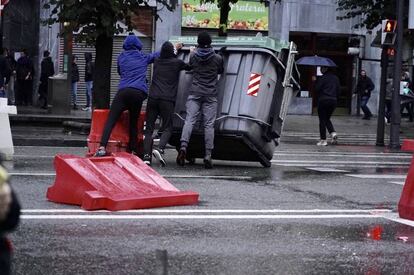 Tres jóvenes vuelcan un contendor durante los incidentes que han rodeado el mitin de Vox en Bilbao. 