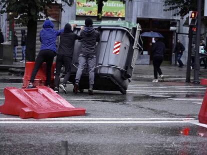 Tres jóvenes vuelcan un contendor durante los incidentes que han rodeado el mitin de Vox en Bilbao. 