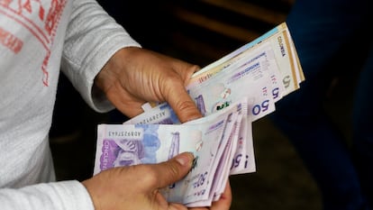 Un hombre cuenta billetes de pesos colombianos.
