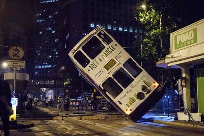 Servicios de emergencia y periodistas miran como un tranva de dos pisos es levantado por una gra tras haber volcado en una carretera principal de Hong-Kong. 