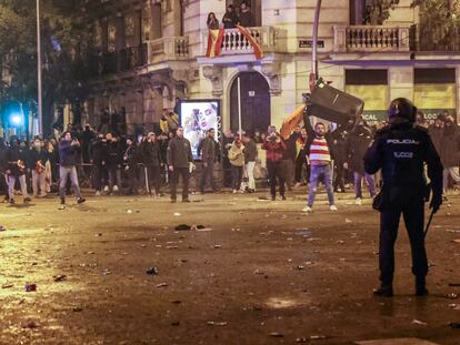 Un hombre coge un contenedor frente a la policía en la confluencia entre las calles de Marqués de Urquijo y Ferraz, este martes. / CLAUDIO ÁLVAREZ