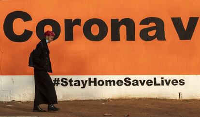 Soweto, Sudáfrica. Una mujer pasea ante un grafiti pidiendo permanecer en casa para evitar contagios por coronavirus.