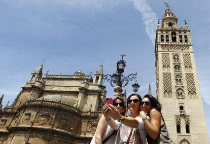 Tres turistas se fotografían con la catedral de Sevilla al fondo.