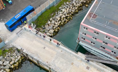 Vista aérea de un autocar y personas llegando al buque 'Bibby Stockholm', reconvertido en centro de migrantes, en el puerto de Portland, este lunes.