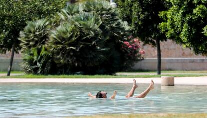 Un joven turista se refresca, este mediodía, en un estanque del jardín del rio Turia en Valencia, donde continúan las altas temperaturas acompañadas por la sensación de bochorno, el 4 de agosto.