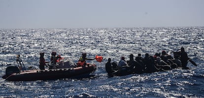 Rescuers on a zodiac hand out life preservers to the people on the sinking boat.