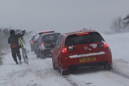 Un hombre junto a su bicicleta cruzan una carretera nevada en Coalville (Reino Unido), el 18 de marzo de 2018.