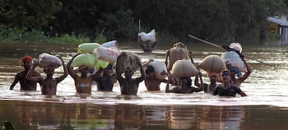 Varias personas llevan sacos de grano sobre sus cabezas por una calle inundada del distrito de Jajpur, ayer en Orissa (India).