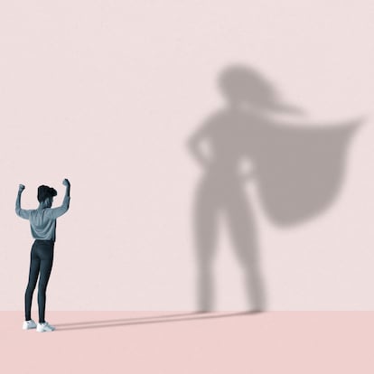 Young woman flexing muscles in front of large superhero shadow on pink background