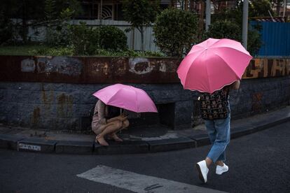 Una mujer revisa su teléfono móvil bajo la lluvia en una calle de Pekín (China).
