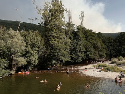 Un hidroavión se dirige el pasado viernes a lanzar agua sobre el incendio entre las localidades navarras de Olloki y Alzuza mientras unos bañistas se dan un respiro en el río Arga a su paso por Irozt.
