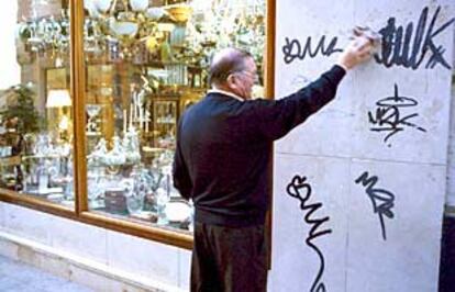 Un comerciante de Orihuela intenta limpiar una pintada en la fachada de su comercio.