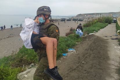 Un miembro del Ejército traslada a un menor inmigrante en uno de los espigones fronterizos de Ceuta, este martes. La llegada masiva de emigrantes de toda edad y condición desde Castillejos, en Marruecos, para atravesar la frontera terrestre con la ciudad española de Ceuta ha continuado por segundo día consecutivo sin aparente respuesta de la policía marroquí