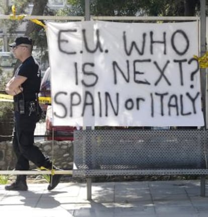 Un policía ante una pancarta en la que se puede leer "Unión Europea, ¿Quién es el siguiente? España o Italia" frente al Parlamento en Nicosia