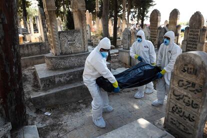 Varios trabajadores trasladan el cadáver de un fallecido por el coronavirus en el cementerio de Salqin (Siria). La pandemia de covid-19 ha registrado en las últimas 24 horas más de 314.000 casos nuevos, con lo que el total se eleva a más de 30 millones de personas contagiadas y supera las 946.000 víctimas mortales, según el balance publicado este viernes por la Universidad Johns Hopkins.