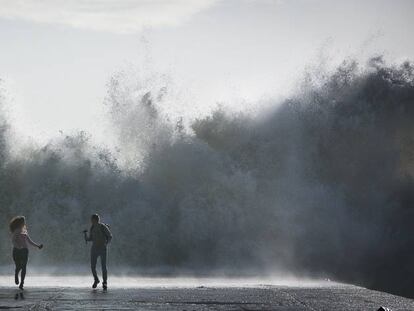 Una pareja corre tras hacerse un selfie mientras pican las olas en el espigón del Bogatell de Barcelona el pasado 23 de enero.