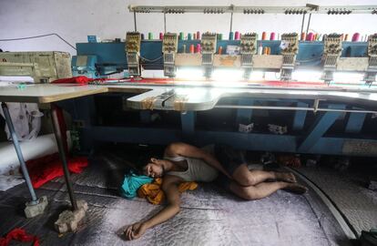 Un trabajador duerme debajo de una máquina de bordar en un taller en Mumbai (India), el 31 de mayo de 2019.