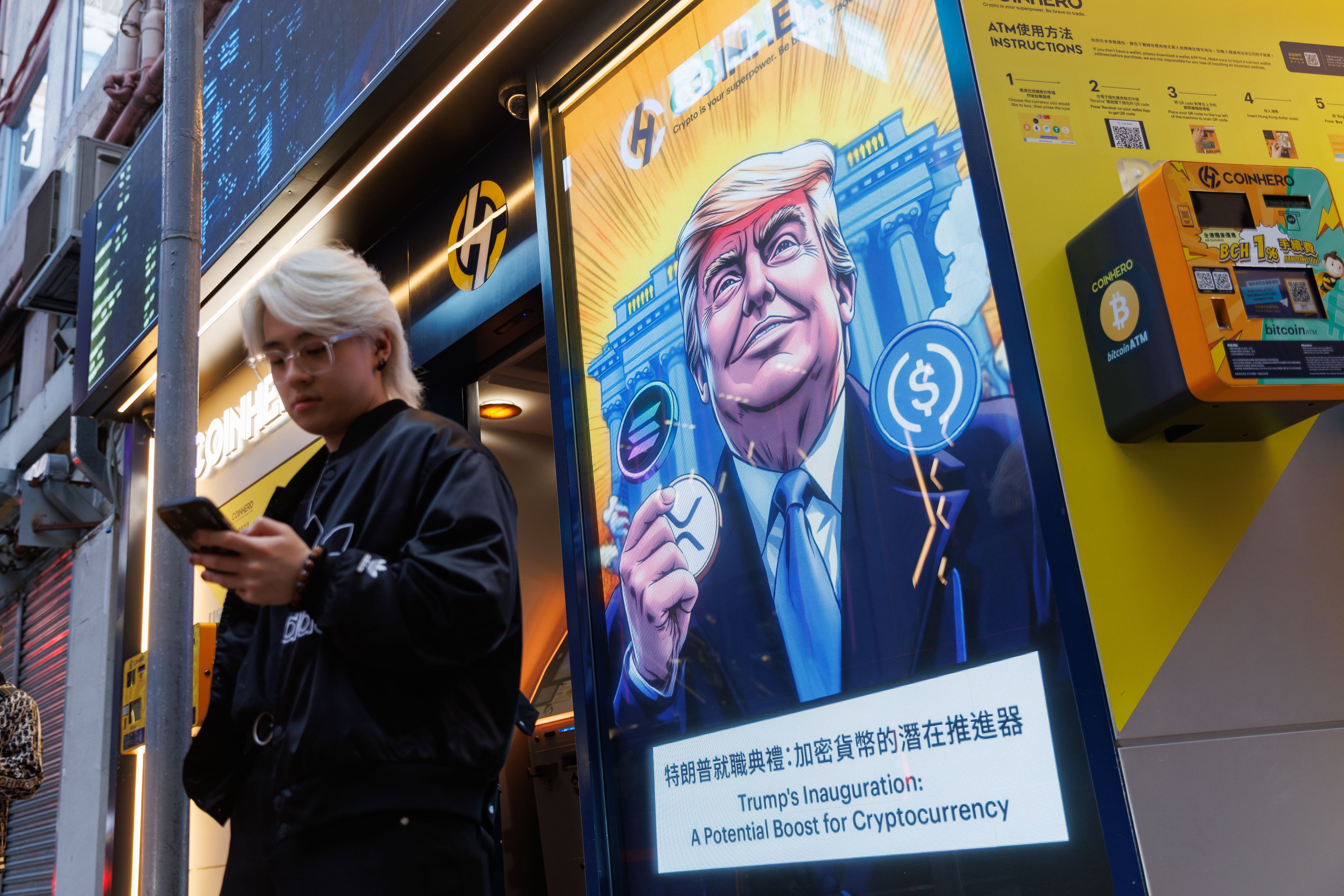 Algunos peatones caminan cerca de un anuncio con el perfil de Donald Trump y las representaciones de algunas criptomonedas.