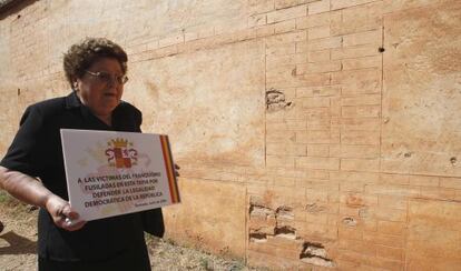 Una mujer, familiar de un fusilado en la tapia del cementerio de Granada, coloca una placa en el lugar en el que fue asesinado.