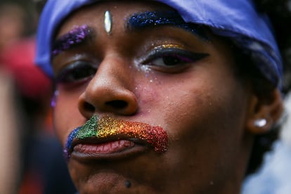 Una persona con un bigote hecho de brillantina, con la bandera con los colores del arcoíris, posa para la cámara durante el desfile del Orgullo LGBT.