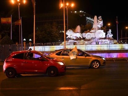 Dos coches pasan esta noche por Cibeles con bufandas y banderas del Real Madrid tras el título de Liga.