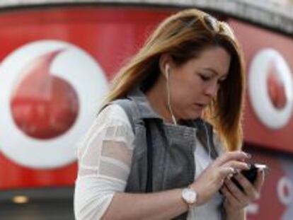 Una usuaria maneja su m&oacute;vil junto a una tienda de Vodafone.