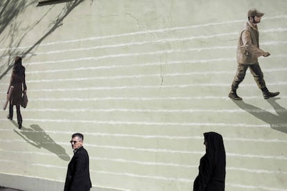 Un pareja pasa por delante de un mural de un hombre y un soldado en Teherán (Irán).