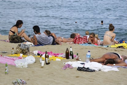 Varios turistas jóvenes en la playa de la Barceloneta junto a botellas de bebidas alcohólicas vacías en la arena.