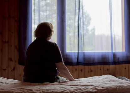Una mujer sentada en su cama frente a la ventana.
