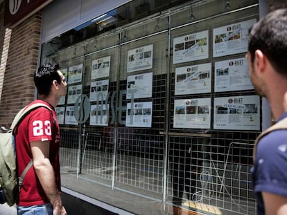 Dos jóvenes miran los anuncios de una oficina inmobiliaria en Madrid.