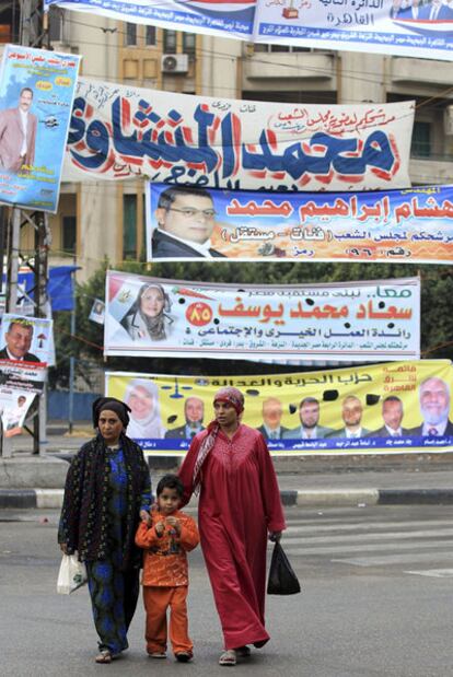 Dos mujeres y un niño pasean junto a pancartas y carteles electorales en las calles de El Cairo.