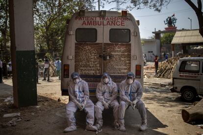 Tres trabajadores agotados, que traen cadáveres para su incineración, sentados en el escalón trasero de una ambulancia dentro de un crematorio, en Nueva Delhi (India).
