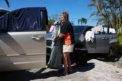 Una mujer seca ropa en las ventanillas de varios coches tras quedarse sin casa por los destrozos causados por el huracán.
