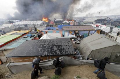 Migrantes transportan sus pertenencias a través de una zona en llamas en 'La Jungla' de Calais, durante el tercer día de evacuación.