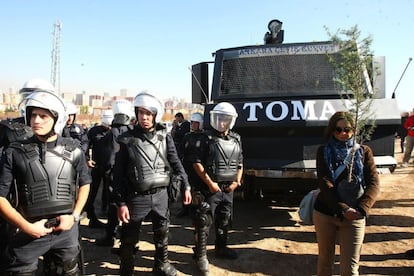 Un manifestante lleva un árbol para plantarlo en el lugar donde se pretende levantar una carretera y que atraviesa una zona boscosa. El proyecto prevé la tala de 3.000 árboles. En la imagen, un grupo de agentes antidisturbios vigilan, junto a un vehículo policial blindado, la manifestación.