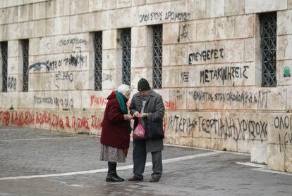 Una pareja de ancianos comprueban las monedas que les quedan junto a la fachada con pintadas de la Universidad de Atenas.