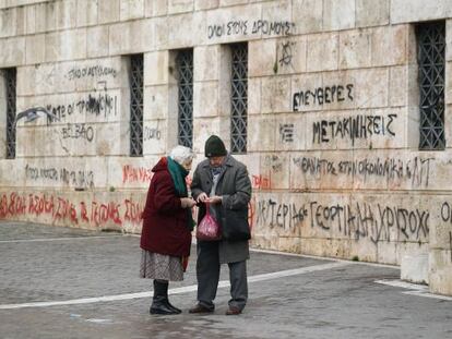 Una pareja de ancianos comprueban las monedas que les quedan junto a la fachada con pintadas de la Universidad de Atenas.