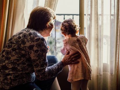Una abuela mira por la ventana junto a su nieta.