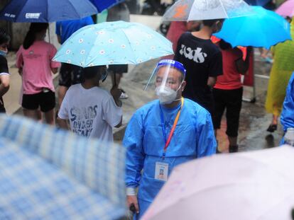 Un trabajador sanitario pasa ante una fila de residentes y turistas, este lunes en la ciudad china de Sanya.