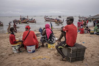 Un grupo de mujeres y jóvenes espera la llegada de los cayucos al puerto de Mbour, en Senegal, tras la jornada de pesca. Mbour es una localidad de tradición pesquera y en la que muchos migrantes han partido a lo largo de la historia en dirección a las islas Canarias.