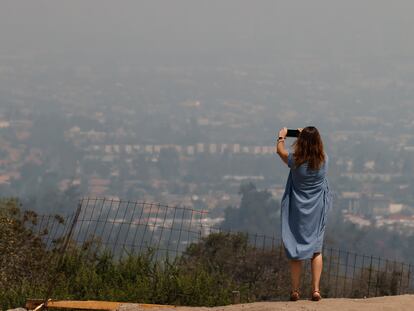 Una mujer toma una fotografía a la ciudad de Santiago cubierta por una nube de humo, Chile.