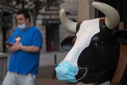 Un joven con mascarilla pasa delante de una escultura de una vaca en Madrid.