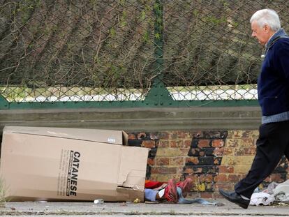 Un hombre pasa por una calle de Buenos Aires, Argentina, junto a una caja en la que una persona sin hogar est&aacute; durmiendo. 