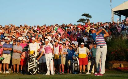 Rickie Fowler juega su golpe de salida en el 18 del playoff ante la mirada de Sergio García, con un palo en la mano.