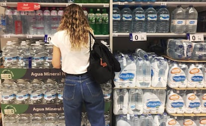 Una joven frente al estante de botellas de agua de plástico en un supermercado en Madrid.