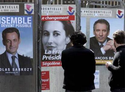 Dos personas observan carteles electorales de tres de los candidatos a la presidencia de Francia, en una calle de París.