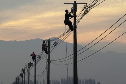 Varios operarios trabajan en unos postes de la luz.