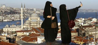 Tres mujeres toman fotografías frente a la Nueva Mezquita, junto al estrecho del Bósforo, en Estambul.