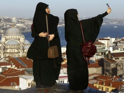 Tres mujeres toman fotografías frente a la Nueva Mezquita, junto al estrecho del Bósforo, en Estambul.
