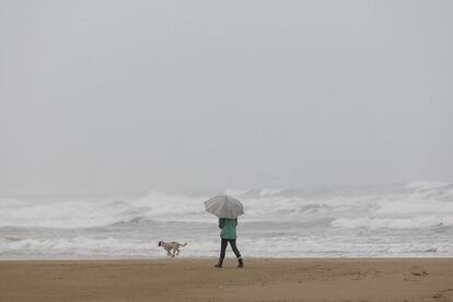 Una mujer pasea bajo la lluvia por una playa de Gandía. Las tres provincias de la comunidad autónoma valenciana están en alerta naranja.